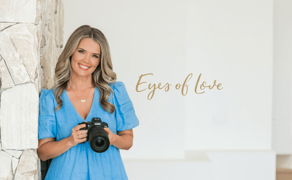 Michelle Swan, renowned Gold Coast photographer, holding her camera and leaning against a sandstone wall in a neutral home setting. She specialises in strategic branding photography, capturing authentic brand imagery that builds trust and connection.