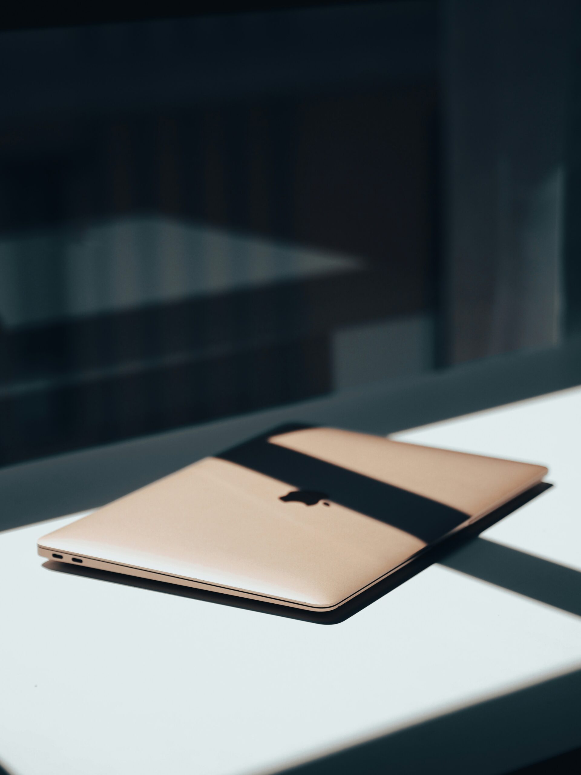 Rose gold Macbook sitting on a desk with shadow falling across it